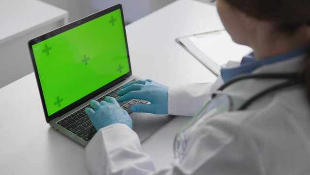 Chroma key template green laptop screen in clinic on table. A diagnostician, focused on efficiency, uses clinical data to accurately diagnose and develop a treatment plan.