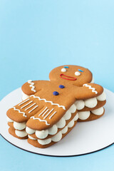 Traditional Christmas honey gingerbread man cake with buttercream filling sprinkled with powdered sugar like a snow flakes on the blue pastel background. Merry Christmas and happy New Year concept.