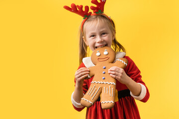 Cute little girl wearing Santa red costume and holding big baked gingerbread man cookie on the yellow background. Portrait of a happy smiling 5 year old girl on the Christmas background