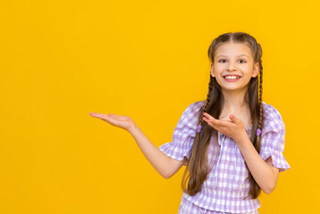 A beautiful little girl points her finger at your advertisement. A happy child. Yellow isolated...