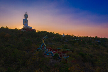 Large Naga Statue and large white Buddha statue with blue sky at Wat Roi Phra Putthabat Phu Manorom, Mukdahan Province, Thailand.