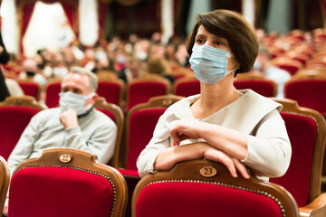Mature man and woman in antivirus mask in theater watching a performance