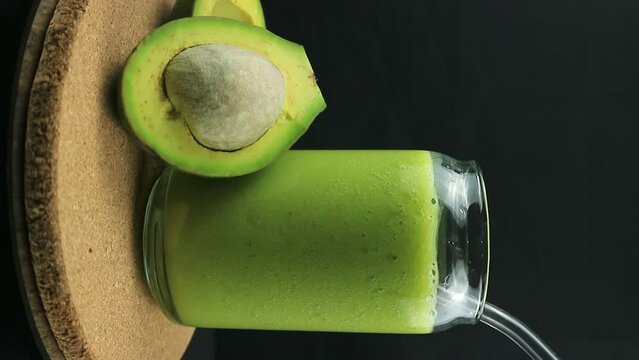 Rotating display of avocado juice on black background. Vertical footage