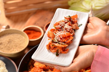Hand holding ready-to-eat kimchi dish in white ceramic plate