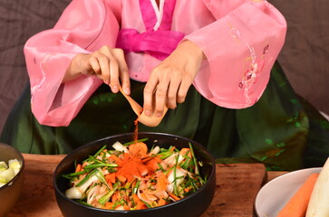 Kimchi preparation. A young Korean woman wearing a pink hanbok is pouring Korean chili powder into a bowl of vegetables for making kimchi. which is a national food preservation