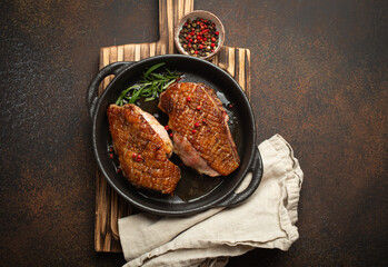 Two roasted duck breast fillets with crispy skin, with pepper and rosemary, top view in black cast...