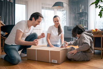 A happy family is eagerly unpacking a large cardboard box with an order from an online store that was delivered to their home. Shopping online with home delivery. - obrazy, fototapety, plakaty