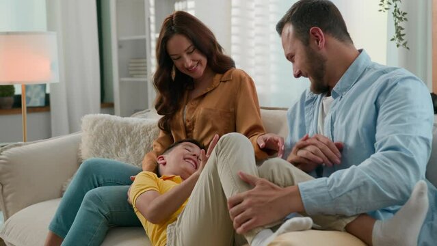 Loving playful parents mother father tickling son kid boy child mum dad tickle playing together sincere laughing enjoying having fun at home couch Bonding Caucasian family happy childhood parenthood