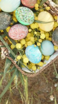 Vertical video. Easter eggs in a basket on the grass, top view. The camera rotates and rises higher.