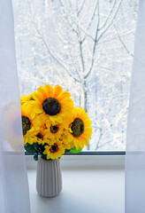 Sunflowers in the winter season on window. Snow-covered trees outside the window. Bright sunflowers against the backdrop of  winter landscape.