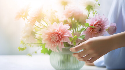 Hands arranging flowers in a vase by bright sunlight