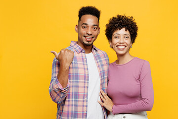 Young smiling couple two friends family man woman of African American ethnicity wear purple casual clothes together point thumb finger aside on area isolated on plain yellow orange background studio.