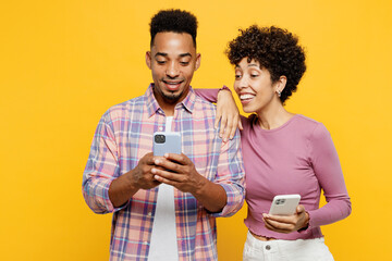 Young smiling couple two friends family man woman of African American ethnicity wear purple casual clothes together hold in hand use mobile cell phone hug isolated on plain yellow orange background.