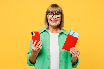 Traveler elderly woman 50s year old wear casual clothes hold passport ticket mobile cell phone isolated on plain yellow background. Tourist travel abroad in free time rest getaway. Air flight concept