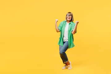 Fototapeta na wymiar Full body elderly blonde woman 50s year old wears green shirt glasses casual clothes doing winner gesture celebrate clenching fists raise up leg isolated on plain yellow background. Lifestyle concept