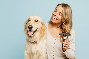 Young smiling fun owner woman wear casual clothes hug cuddle best friend retriever dog hold grooming brush isolated on plain pastel light blue background studio portrait. Take care about pet concept.