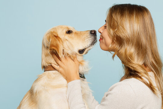 Side profile view smiling young owner woman with her best friend retriever wear casual clothes kiss hug cuddle dog isolated on plain pastel light blue background studio. Take care about pet concept.