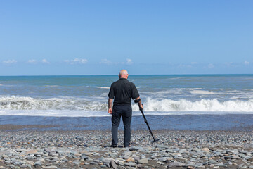 An old man searches for lost jewelry on the  with a metal detector. Metal detecting sea. Hobby active age concept.
