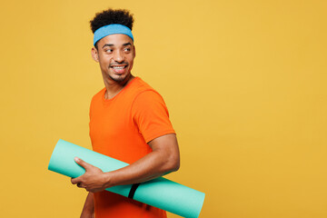 Sideways young fitness trainer sporty man sportsman wear orange t-shirt hold in hand yoga mat look...