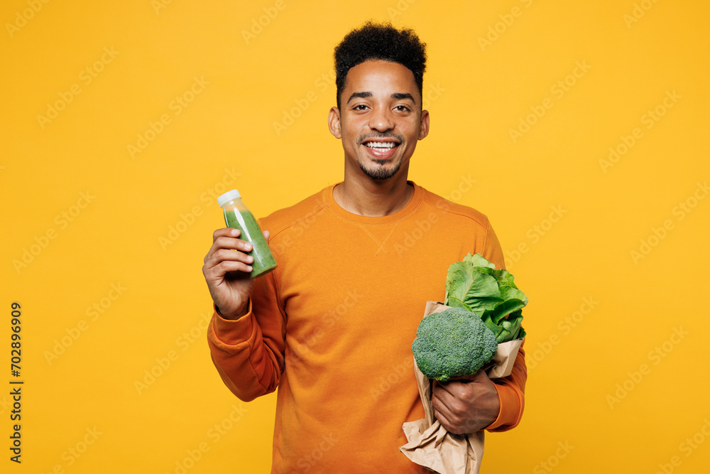 Wall mural Young man wear casual clothes hold show juice green vegetable smoothie as detox diet, greenery herbs isolated on plain yellow background. Proper nutrition healthy fast food unhealthy choice concept..