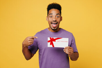 Young shocked man of African American ethnicity in purple t-shirt casual clothes hold point finger...