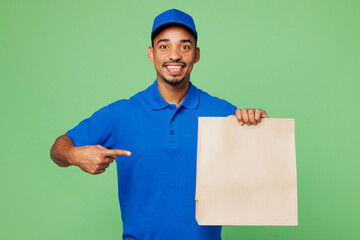 Delivery guy employee man wear blue cap t-shirt uniform workwear work as dealer courier hold point finger on clear blank paper takeaway bag mock up isolated on plain green background. Service concept.