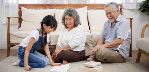 Fotobehang Asian senior couple watching granddaughter doing homework on the floor. Grandparents love and support little girl. Healthy living and lifestyle insurance © winnievinzence