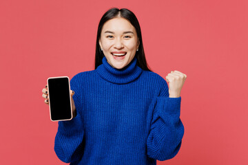 Young smiling happy woman of Asian ethnicity wear blue sweater casual clothes hold use blank screen...