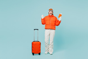 Traveler winner skier woman wear padded windbreaker jacket ski goggles mask hold passport ticket bag isolated on plain blue background Tourist travel abroad free time rest getaway. Air flight concept