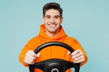 Young smiling happy man he wears orange hoody casual clothes hold steering wheel driving car look...