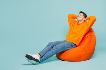 Full body side view minded young man he wears orange hoody casual clothes sit in bag chair hold...