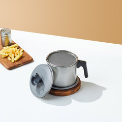 A stainless steel oil tray, with fried fries and sausage on top and on a wooden tray, on a white and beige colored background.