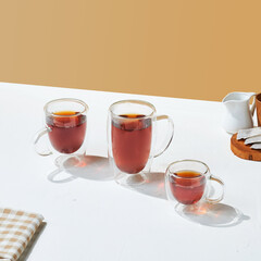 a variety size of transparent double wall glass with tea inside it, on a white and beige colored background.