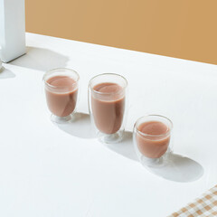 a variety size of transparent double wall glass with chocolate milk inside it, on a white and beige colored background.