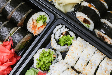 Takeaway sushi background. Uramaki California roll and futomaki. Japanese food isolated on black. Black sushi takeaway box closeup. Different various types of sushi. Lunch box texture. Sesame seeds.