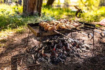 Barbecue at a picnic with grilled kebabs. Half-cooked pieces of pork meat on skewers on an old iron portable grill over coals