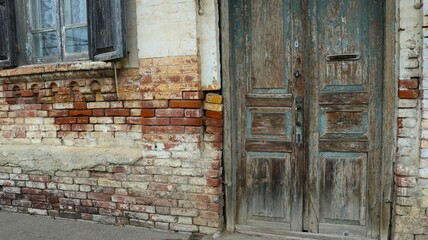 fragment of the external wall of an ancient house with a shabby wooden door and a rickety window, with a destroyed brick corner as an old texture