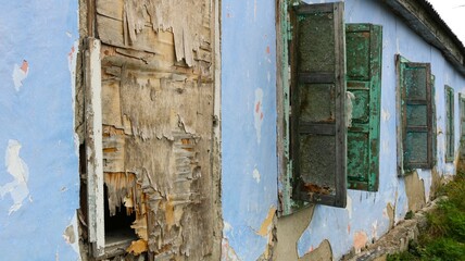 view of the facade of an old abandoned house with windows boarded up and covered with plywood and rickety shutters in a receding perspective, a fragment of a dilapidated residential building