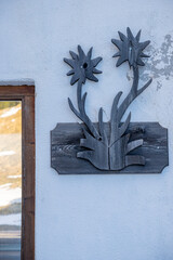 Wall decoration on a whitewashed, weathered wall: wood carving depicting two edelweiss.  Part of a...