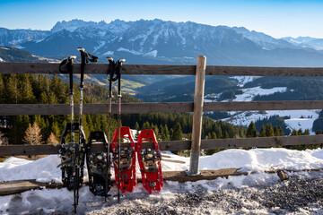 Snowshoeing in a winter landscape: snowshoes and walking sticks lean against a wooden fence. ...