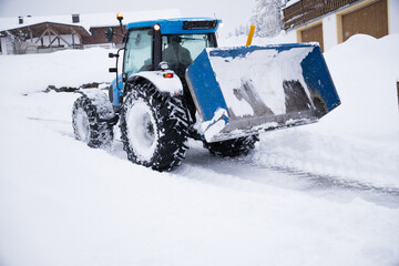 Onset of winter. Rear view of blue tractor with loader and snow chains clearing snow.  Winter landscape