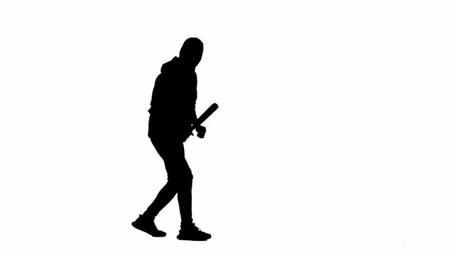 Black silhouette of thief on isolated white background. A male robber in hoodie and balaclava walks with a wooden bat in his hands, preparing to commit a crime. Side view.