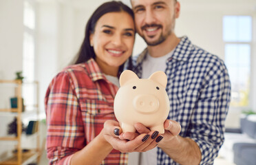 Close up captures a couple hands jointly hold a piggy bank at home. Family smiles radiate joy and...