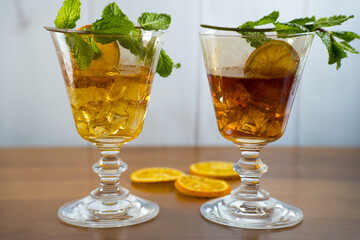 Two decorative glasses. One filled with Blueberry Liqueur and the other with Mandarin Liqueur. Both decorated with ice cubes, orange slice and mint sprig