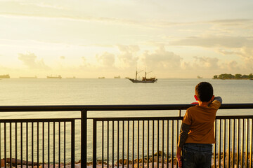 Maritime marvel: Rear view of a boy enjoying the view of a wooden ship sailing on the beach in the...