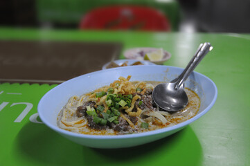 Khao Soi (Thai coconut coconut curry noodle soup) on green table.