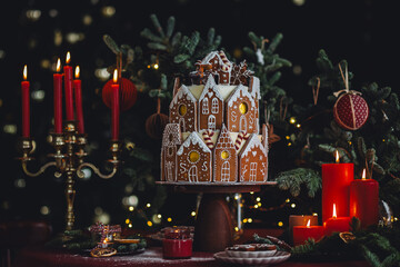 Beautiful traditional homemade gingerbread house. Celebration of Christmas and Happy new year at home. Festive mood, cozy atmosphere, red candles, fir tree branches. Elegant decor
