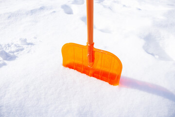 photo of a bright orange shovel in the snow on a frosty sunny winter day. Snow removal after a...