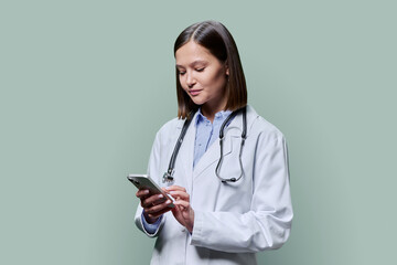Young female doctor using smartphone, on green studio background