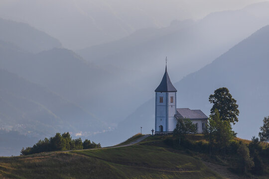 Church of Saint Primoz in Jamnik village, Slovenia, Europe. The church is on the ridge of the mountains. Sunrise, mountain peaks in the background.